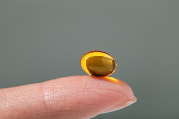 Female hand holding a small yellow capsule of nutritional supplement . Food supplement, vitamin D,...