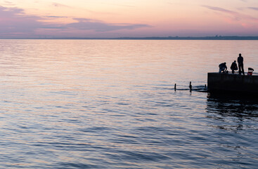 Ships on horizon stand in roadstead. Fishing on sea, colorful morning sunrise, people on pier fish,...