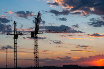 Silhouette construction cranes on background beautiful sky with clouds, bright colorful sunset