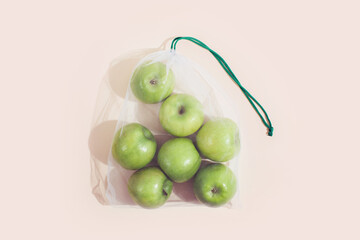 Reusable packaging of products by weight. Apples in a reusable bag close up on a pink background