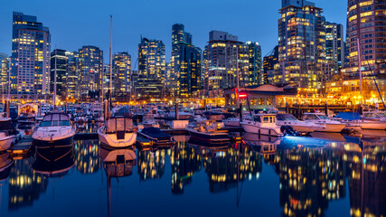 Night exposure of downtown Vancouver, British Columbia, Canada. One of the most vibrant cities in North America. Blue clear sky with water reflections lights trail, stars, and glitters.
