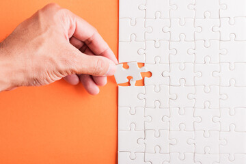 Top view flat lay of hand-holding last piece white paper jigsaw puzzle game last pieces put to...