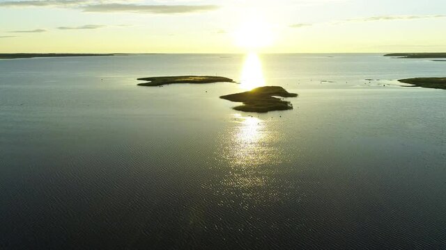 Beautiful Serene Scenery, Sunset Landscape With Rippling Water Texture, Gleaming Sun Reflection, Yellow Sky Horizon And Small Flat Islands, Aerial Drone Tilt Down Backward Motion