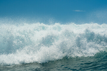 Fototapeta premium White foamy water on a tropical turquoise breaking ocean wave with blue sky background.