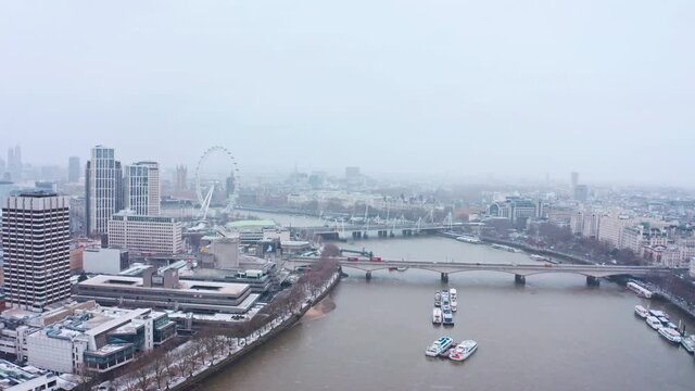 Cinematic rotating aerial shot of snow falling London waterloo bridge south bank London eye