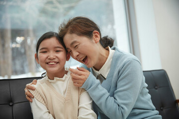 Senior woman hugging granddaughter while sitting on sofa at home