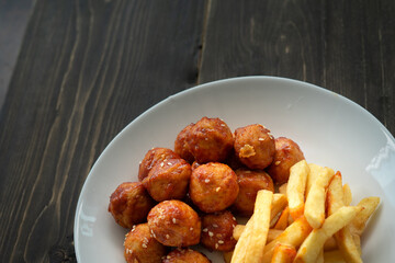 Spicy coated meatballs with spicy sauce served with fried potatoe fries. Korean style snacking.