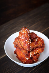 Chunks of fried chicken in a spicy sauce and sesame seeds. Food Korean cuisine on a wooden background.