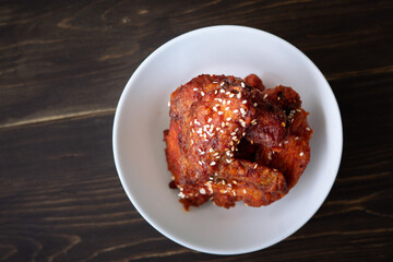 Chunks of fried chicken in a spicy sauce and sesame seeds. Food Korean cuisine on a wooden background.