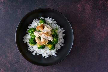 Black food bowl with steamed rice, roasted broccoli and grilled check breast
