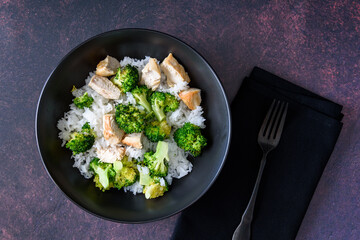 Black food bowl with steamed rice, roasted broccoli and grilled check breast
