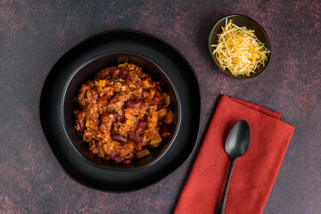 Black bowl of spicy chili con carne on a rustic moody background
