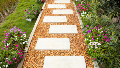 Selective focus shot of white stone path with yellow and brown gravel in colorful flower garden and...