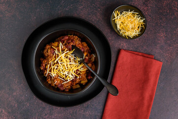 Black bowl of spicy chili con carne on a rustic moody background
