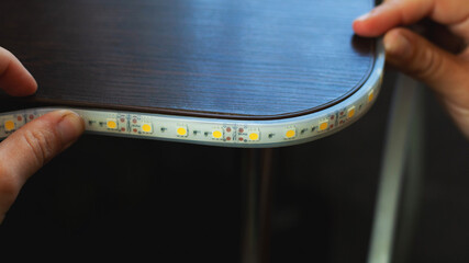 the master glues the LED strip into the niche of the shelf from the cabinet for...
