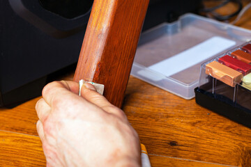 master wipes a scratch on a leg from wooden furniture restoration repair