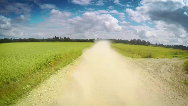 Countryside nature, remote POV drive back view, gravel dusty road, green farm fields, blue sky clouds summer day, car travel gopro point of view