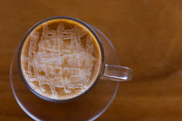 Soft focus Top view close up of ice latte coffee in a white ceramic cup on a wood table background. Focus selective creamy top of glass