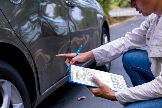  Insurance agent writing on clipboard while examining car after accident claim being assessed and processed. Insurance man check for damage on side door car after accident. Transportation concept