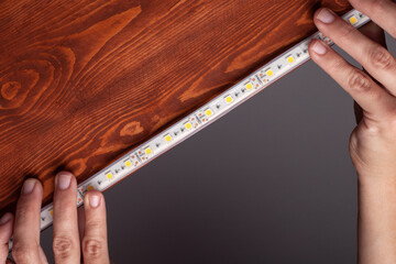 the master glues the LED strip into the niche of the shelf from the cabinet for lighting.installation of diode lighting tape