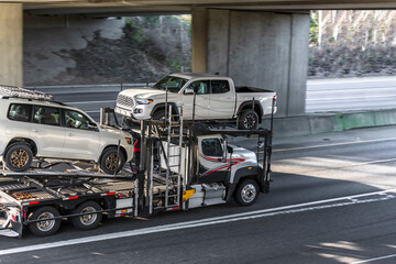 Big rig semi truck car hauler transporting cars on two level semi trailer driving on the highway...