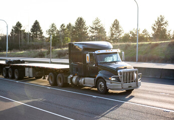Black big rig low cabin semi truck with two empty flat bed semi trailers running on the highway...