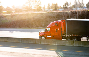 Bright orange big rig semi truck tractor transporting cargo in black covered semi trailer running...