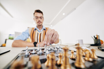 Intelligent young university student moving queen piece when playing chess, selective focus