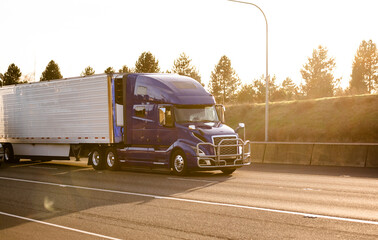 Dark blue big rig semi truck with grille guard transporting refrigerated semi trailer with frozen...