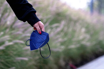 Female hand holding a protective face mask in nature, empty space for text, new beginning