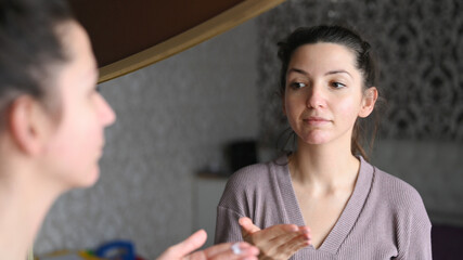 A young caucasian woman applies a cream to the skin in front of the mirror. Morning skin care treatments. Awakening from sleep concept