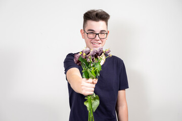 a young man with glasses holds out a bouquet of wilted flowers and smiles. the concept of greed and...