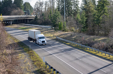 White big rig semi truck transporting cargo packed in container running on the divided highway road...