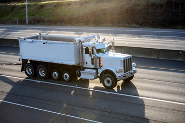 Working horse big rig tipper truck with two trailers running on the highway road with sun light