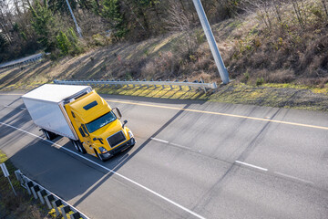 Yellow high cabin long haul big rig semi truck with refrigerator semi trailer running on the...