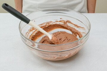 Chocolate cake batter in a glass bowl close up on kitchen table.