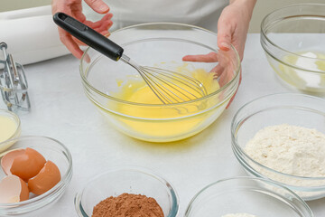 Fototapeta na wymiar Chocolate cake step by step recipe. Woman whisks egg yolks with sugar in a glass bowl