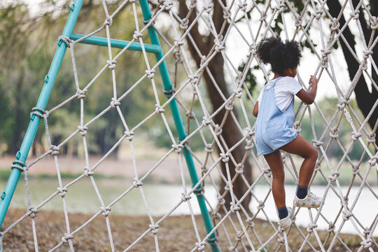 Little African American curly hair girl playing on park playground in spring or summer season. They enjoy climbing on the rope equipment.