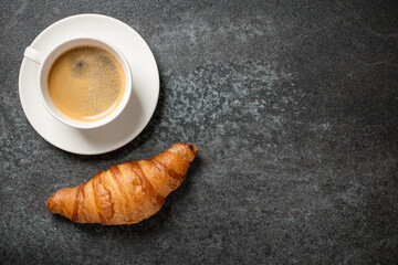 Cup of coffee and fresh croissant on black table