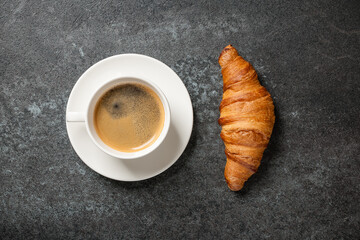 Cup of coffee and fresh croissant on black table
