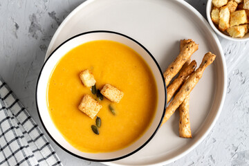 Top view of Pumpkin, carrot cream soup in a bowl. with croutons, pumpkin seeds and bread sticks.