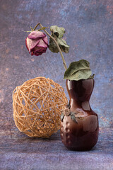 Vase en argile avec glaçure avec des fleurs et une rose sèche dedans, et une boule en osier de...
