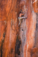 A strong man climbs a beautiful orange rock.