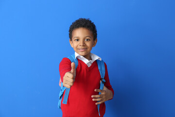 Little African-American schoolboy showing thumb-up gesture on color background