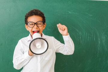 Little African-American schoolboy with megaphone near chalkboard in classroom