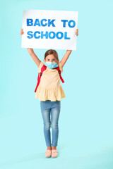 Little girl in medical mask holding placard with text BACK TO SCHOOL on color background. Coronavirus epidemic