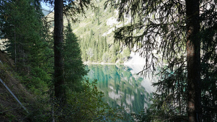 Kolsay lake among green hills and mountains. The mountain lake is surrounded by green forest, tall coniferous trees, grass and bushes. Clean water is like a mirror. Tourists swim on boats. Kazakhstan