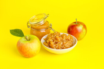 Jar and bowl with sweet apple jam on color background