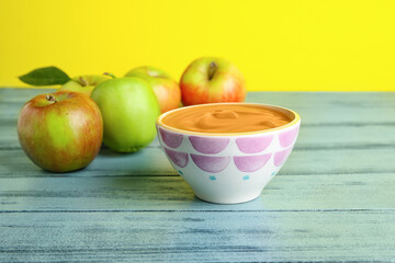 Bowl with sweet apple jam on wooden table against color background