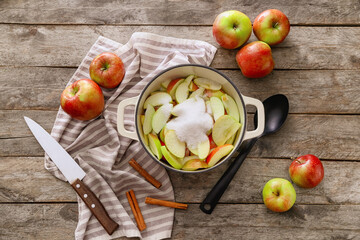 Cooking pot with cut apple and sugar on wooden background